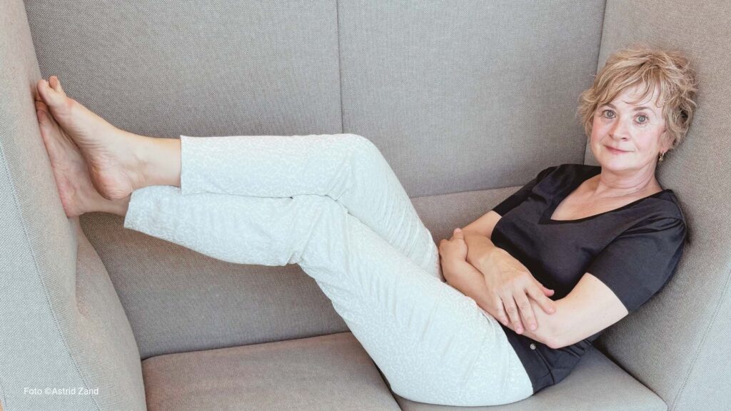 Frau sitzt auf einem Sofa, die Füße hochgelegt, blickt nachdenklich – Angst im Veränderungsprozess bewältigen